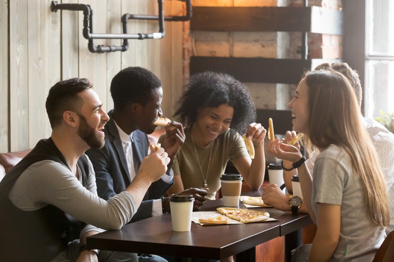 Multiracial happy young people laughing eating pizza together in
