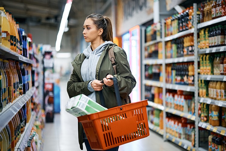 Young woman looks at products of shelves while buying in supermarket.